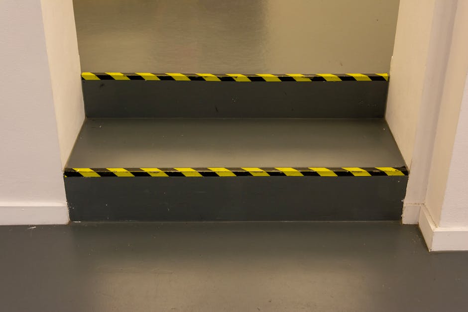 A view looking down the central spiral staircase of a residential building, showing the curved handrail with a wooden top rail and black metal balusters. The staircase has grey steps with black anti-s